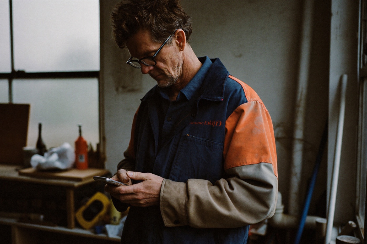 Ondernemer in zijn werkplaats kijkt op zijn telefoon.